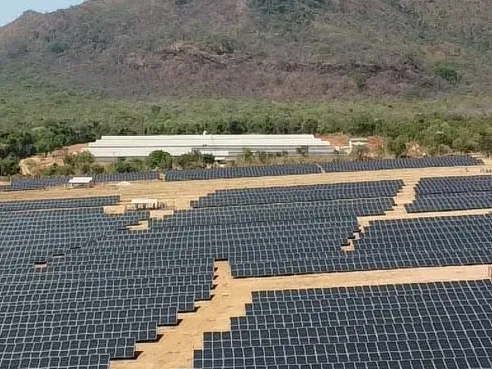Grande usina fotovoltaica em solo, com a serra ao fundo.